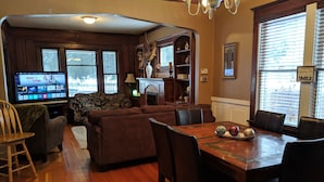 A cozy living room with a wooden floor, a sofa, a TV, and a dining area with a table and chairs. - Walking distance everywhere, yard, front porch and hot tub! (Coeur d'Alene)