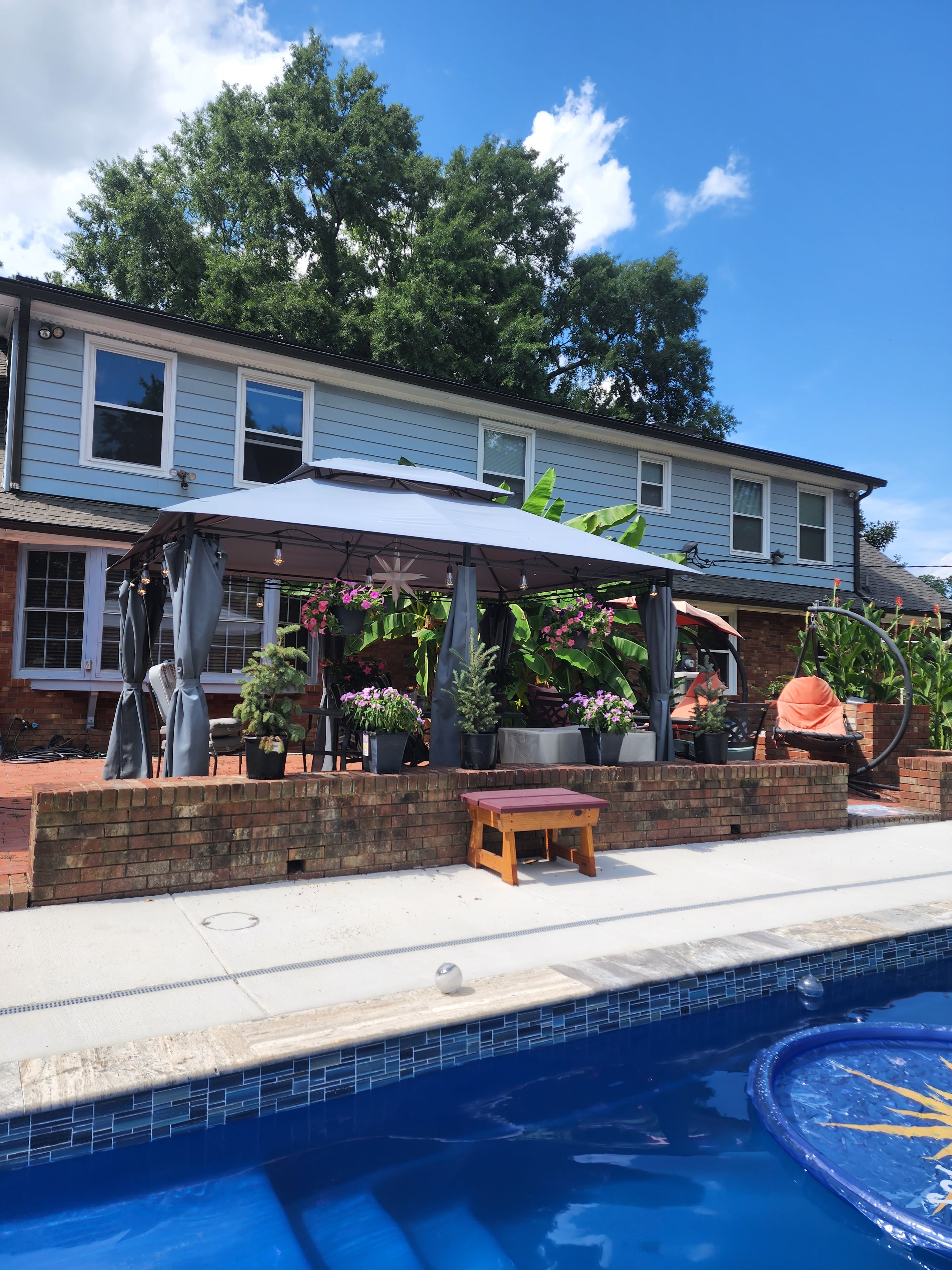 A residential property with a swimming pool, a covered patio area with seating, and a brick wall.