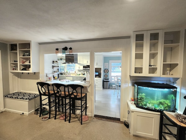 A kitchen with white cabinets, a dining table with chairs, a fish tank, and a window with a view.