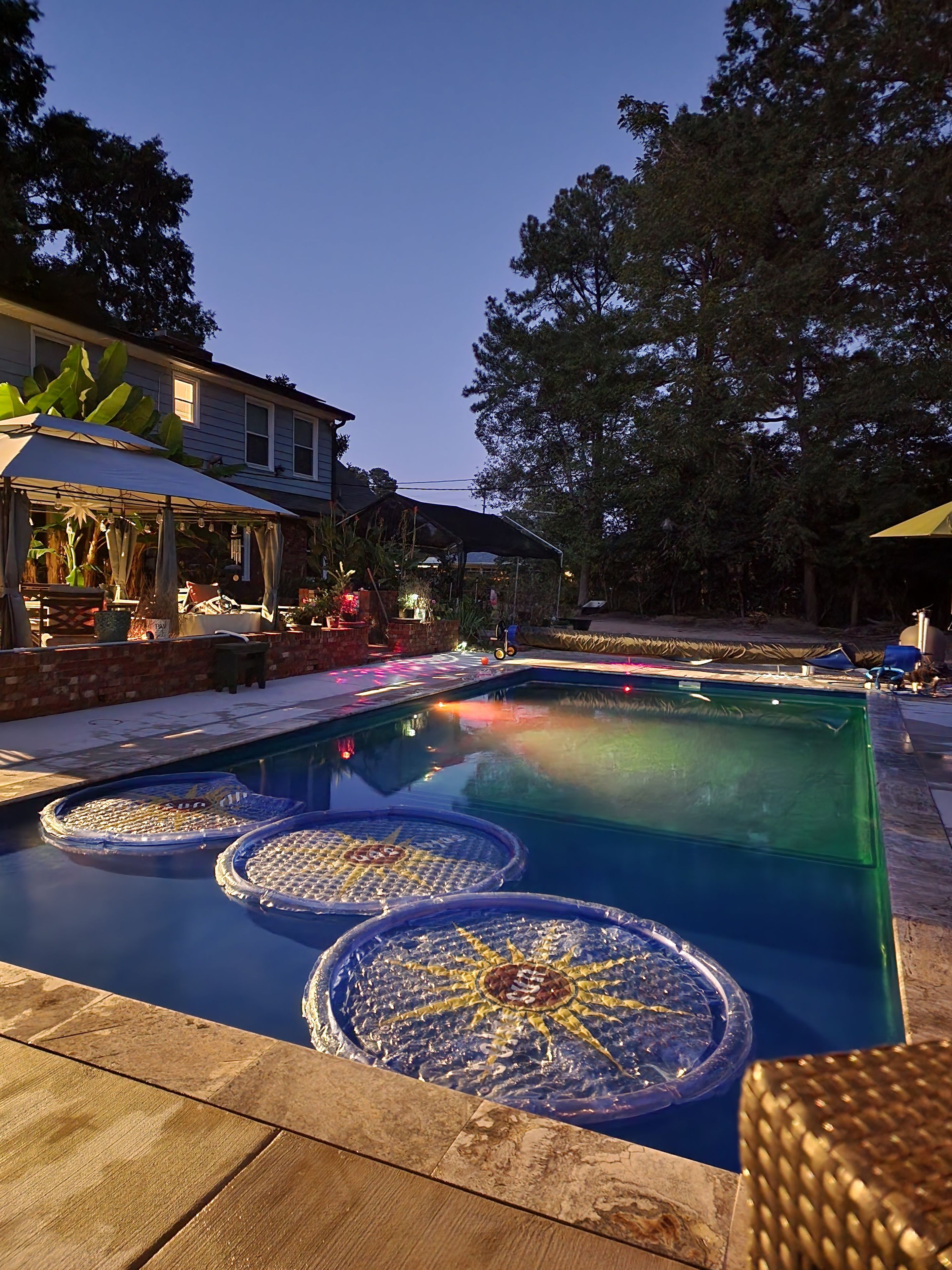 A swimming pool with floating platforms and a covered seating area with plants and outdoor furniture.
