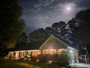A house with a brick exterior, a visible garage, and a well-lit front yard at night.