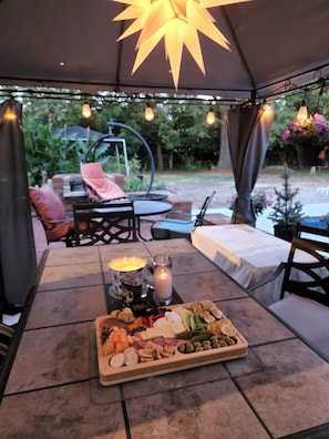 An outdoor dining area with a table set for a meal, surrounded by chairs and a hanging light fixture.