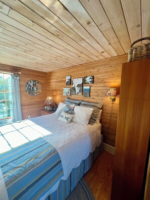 A cozy wooden cabin bedroom with a bed, pillows, a nightstand, and wall art.