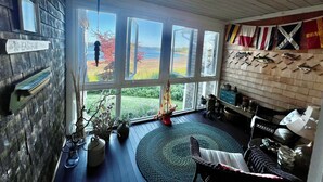 A room with large windows, a wooden ceiling, and a wall decorated with flags. - Oceanfront - 3 Acre Private Beach Property, See Whales & Eagles from the Deck (Eastport)
