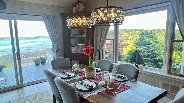 A dining area with a wooden table, six chairs, and a view of the ocean. - Oceanfront - 3 Acre Private Beach Property, See Whales & Eagles from the Deck (Eastport)
