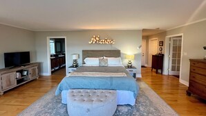 A bedroom with a large bed, a television, a dresser, and a bathroom visible through an open door. - Oceanfront - 3 Acre Private Beach Property, See Whales & Eagles from the Deck (Eastport)