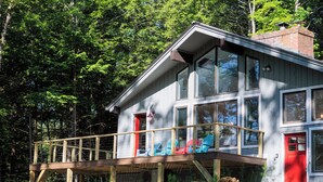 A cabin with a deck, large windows, and a red door. - The Real Vermont All Seasons Get-Away Home - Part of Queche Lakes Country Club (Quechee)