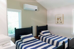 A bedroom with two beds, a window, an air conditioning unit, and a framed picture on the wall.