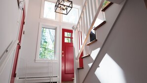 A staircase leading to a red door with a white railing, a radiator, and a hanging light fixture. - The Real Vermont All Seasons Get-Away Home - Part of Queche Lakes Country Club (Quechee)