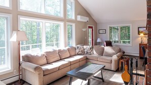 A spacious living room with large windows, a ceiling fan, and a fireplace. - The Real Vermont All Seasons Get-Away Home - Part of Queche Lakes Country Club (Quechee)