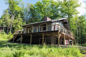 A two-story cabin with a balcony, surrounded by forest.