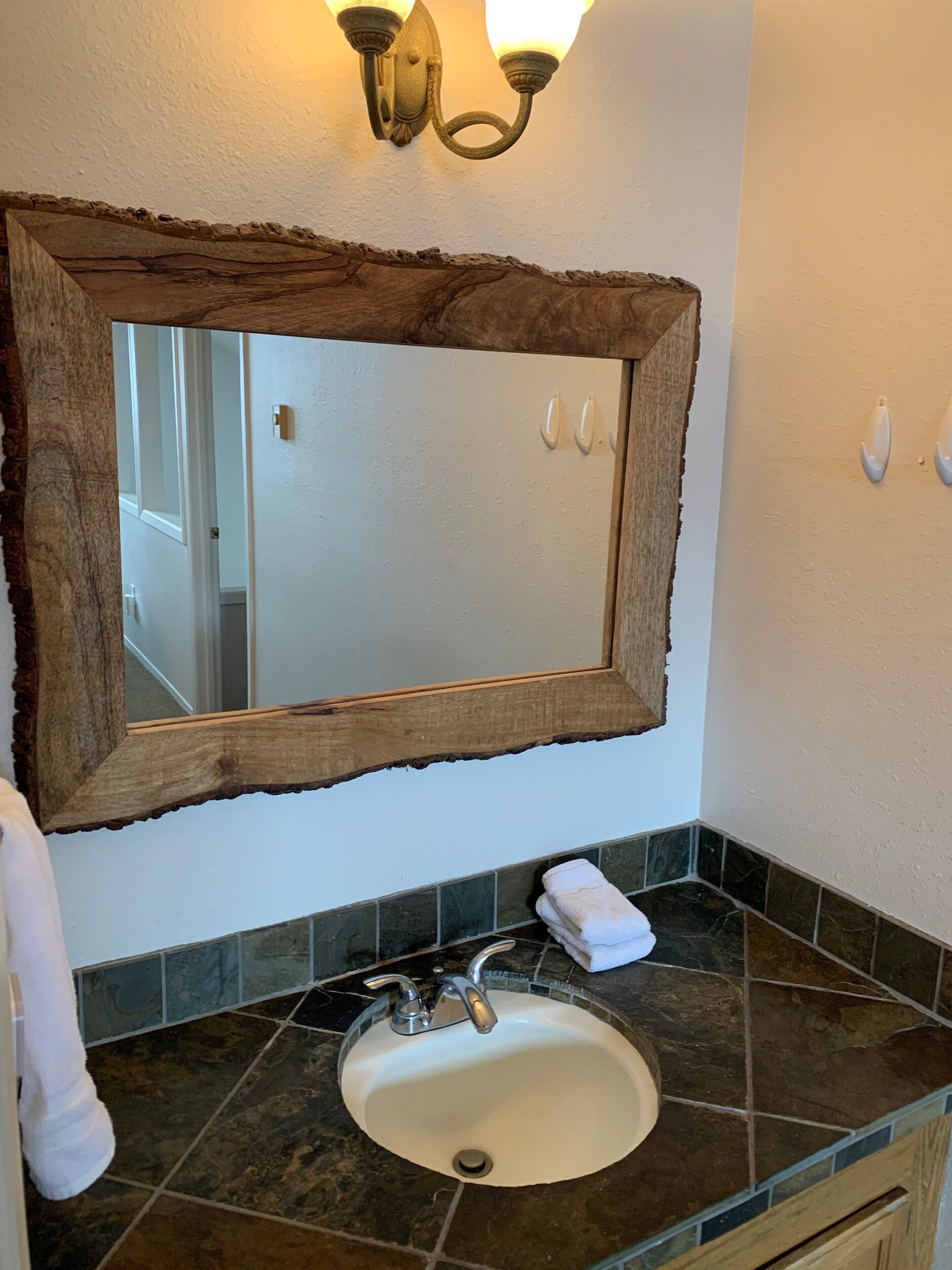 Une salle de bain avec un miroir rustique encadré en bois, un lavabo blanc et une serviette posée sur le comptoir.