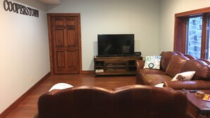 Ein Wohnzimmer mit einem braunen Ledersofa, einem Fernseher auf einem Holzschrank und einer Tür mit der Aufschrift 'COOPERTOWN'.