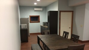 Ein Essbereich mit Holztisch und -stühlen, eine kleine Küchenzeile mit Kühlschrank und Mikrowelle sowie eine Tür zu einem anderen Raum.