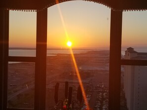 Panorama al tramonto da una finestra su una città con edifici e un corpo d'acqua.