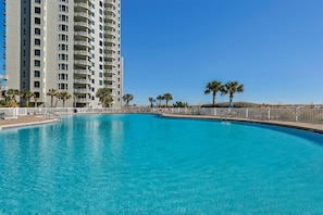 A swimming pool with a clear blue water, surrounded by a white fence, and a tall building with balconies in the background.