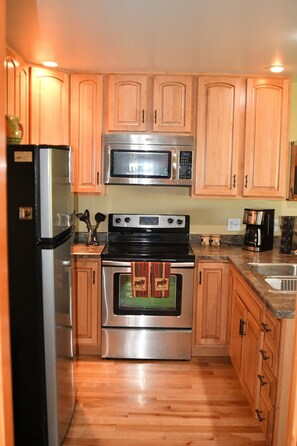 A kitchen with wooden cabinets, a stainless steel refrigerator, a microwave, a stove, and an oven.