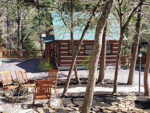 Un chalet rustique avec un toit végétalisé, entouré d’arbres et de chaises en bois.
