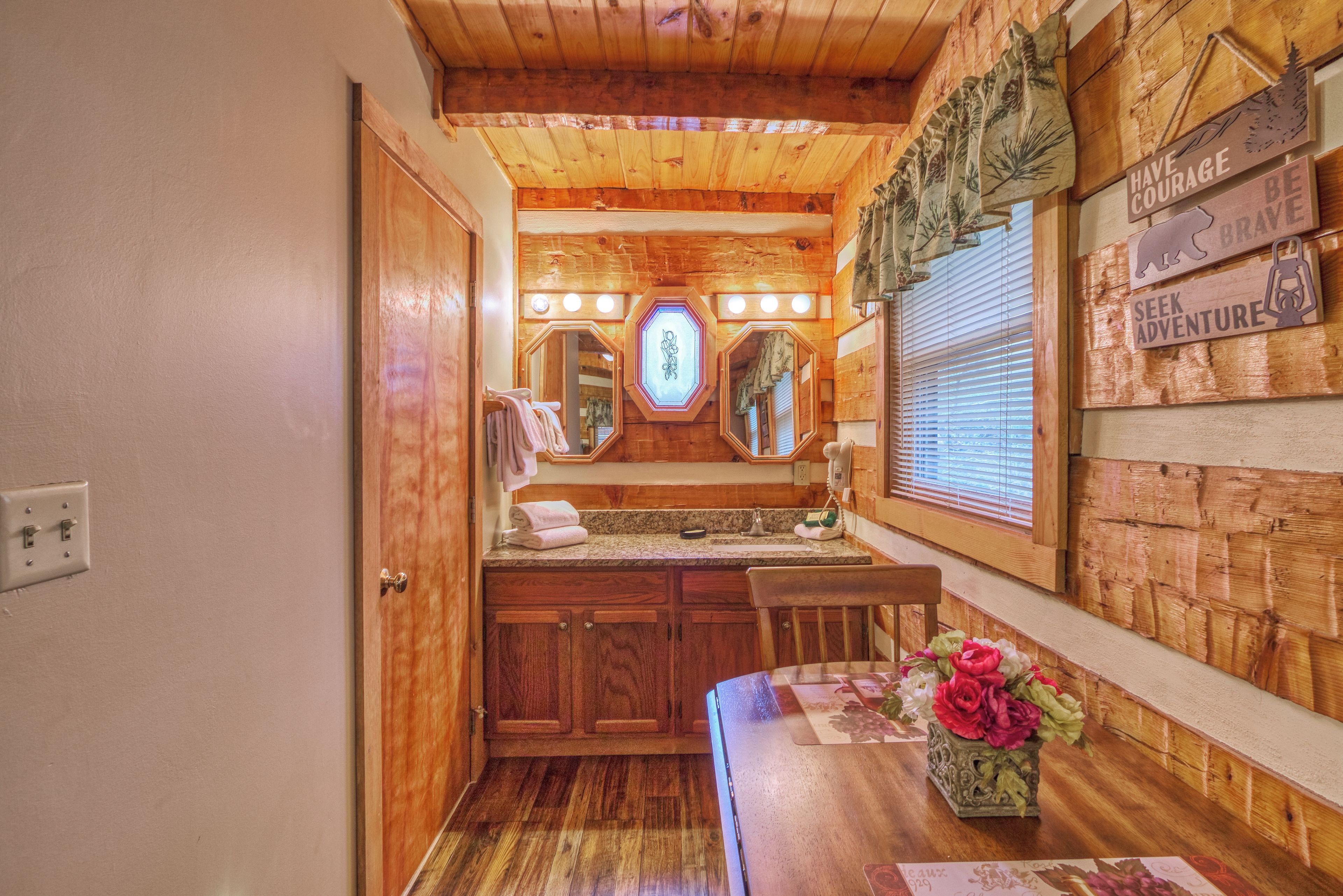 Une salle de bain avec des murs en bois, un meuble-lavabo avec un miroir, un évier et une fenêtre avec des stores.