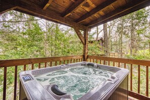 Ein Whirlpool unter einer Holzterrasse mit Blick auf ein bewaldetes Gebiet.