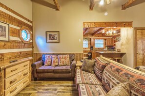 Una sala acogedora con una pared de madera, un sofá marrón, un sofá estampado y un mueble de madera.