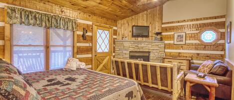Una habitación de cabaña de madera con una cama, una chimenea, un televisor y un balcón.