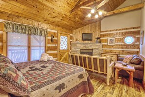 Une chambre dans un chalet en bois, équipée d’un lit, d’une cheminée, d’une télévision et d’un balcon.