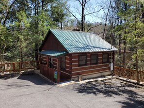 Eine rustikale Holzhütte mit einem Metall-Dach, umgeben von einem Holzzaun, inmitten eines bewaldeten Gebietes.
