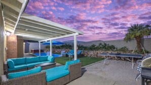 Um pátio externo com área de estar coberta, piscina e churrasqueira.