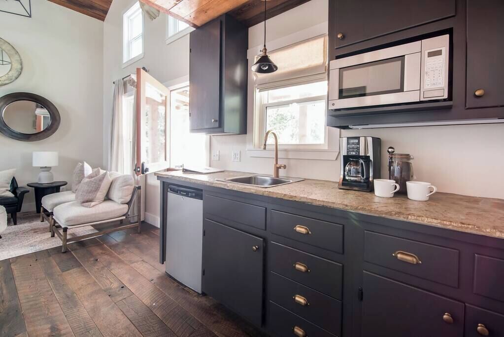A kitchen with dark cabinets, a dishwasher, a coffee maker, and a window above the sink.