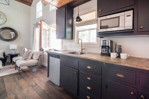 A kitchen with dark cabinets, a dishwasher, a coffee maker, and a window above the sink. - Modern Guesthouse w/ Hot Tub + Fireplace (Fredericksburg)
