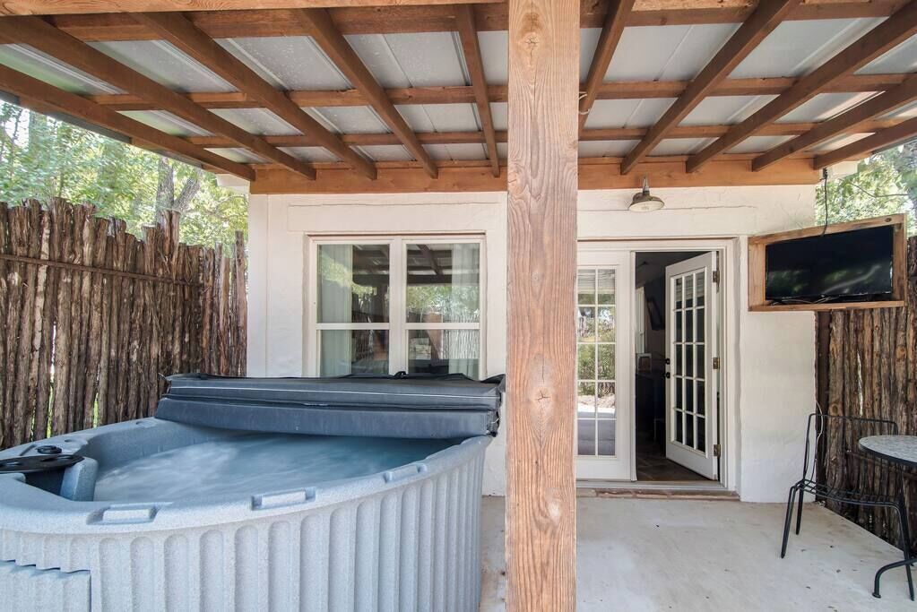 A covered outdoor area with a hot tub, wooden beams, a television, and a door leading to an interior space.