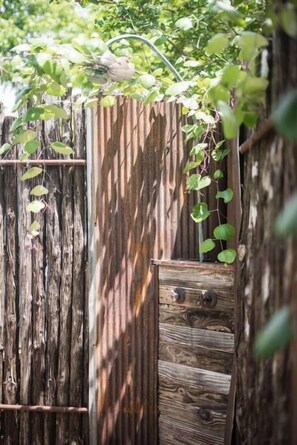 A rustic wooden fence with a small opening, surrounded by lush greenery. - Modern Guesthouse w/ Hot Tub + Fireplace (Fredericksburg)