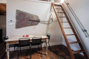 Ein Essbereich mit einem Holztisch, schwarzen Stühlen, einer Metallwanddekoration und einer Holzleiter an der Wand.