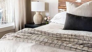Uma cama com colcha estampada, cabeceira de madeira, luminária de mesa e uma revista no chão.