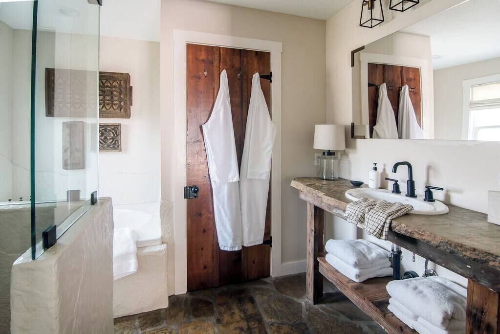 Un baño con bañera, una puerta de madera, un espejo y un lavabo con toallas.