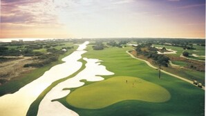 Un parcours de golf avec des bunkers de sable, un obstacle d’eau et un ciel dégagé.