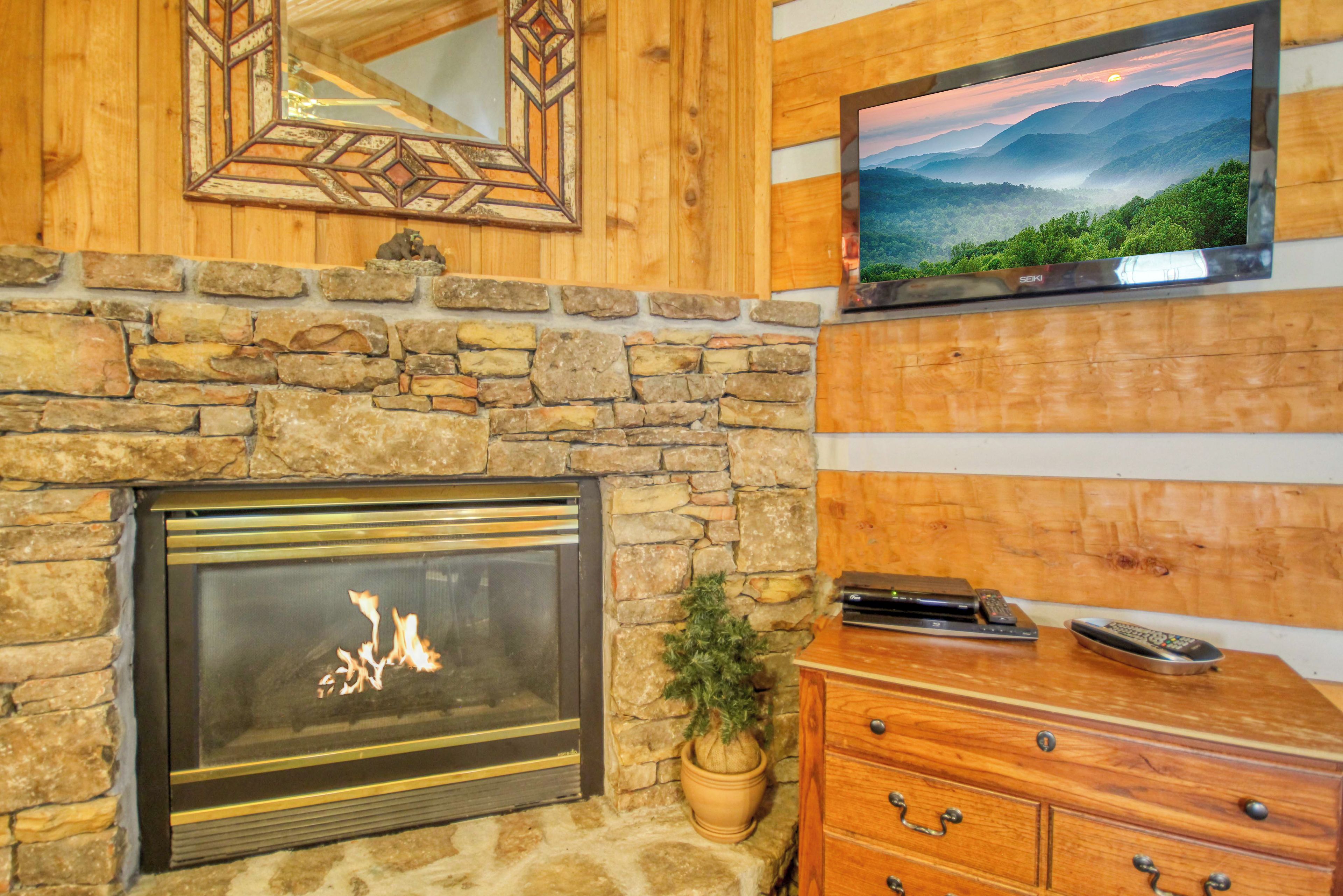 A stone fireplace with a modern TV above it, wooden paneling, and a wooden dresser with a plant.