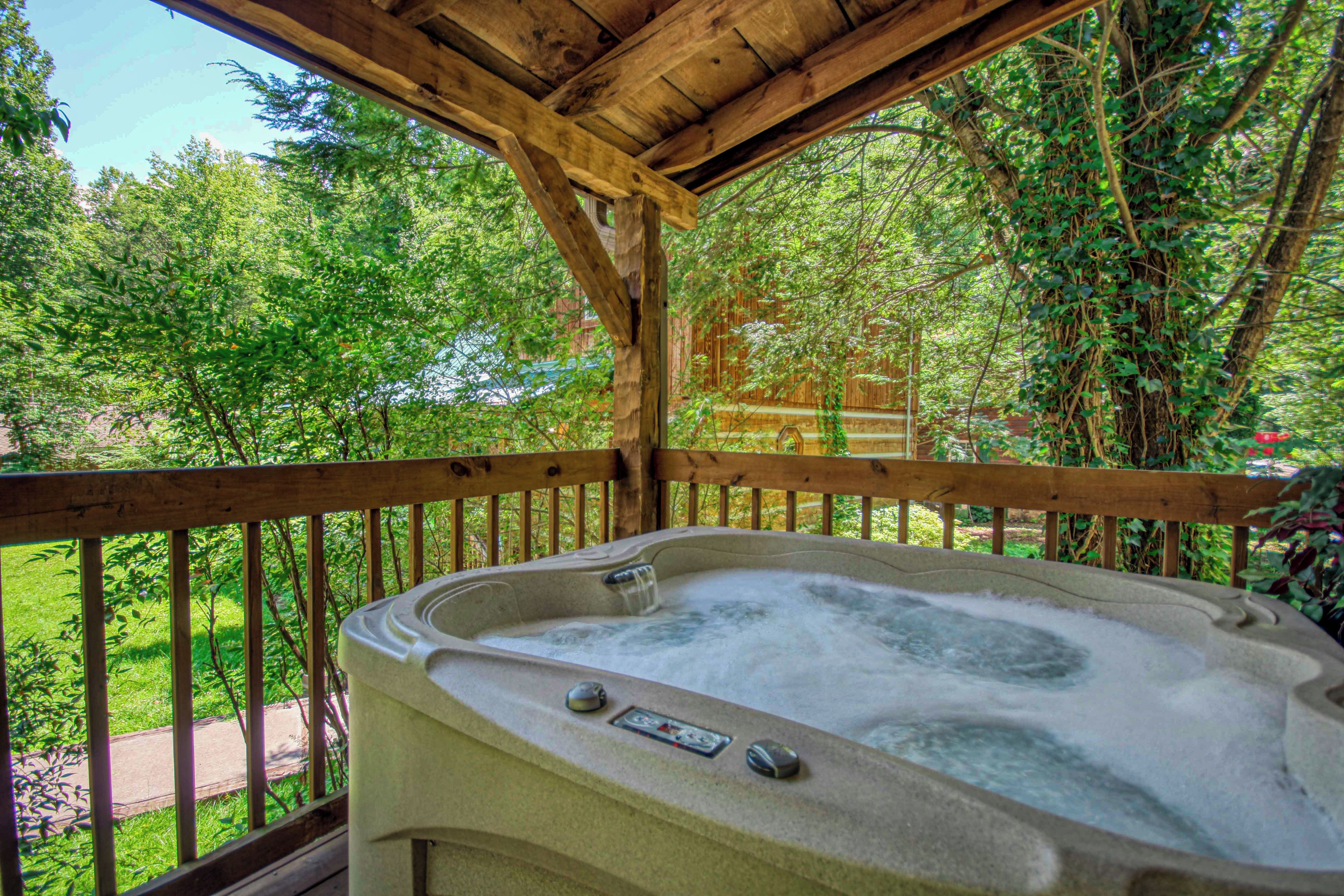 A hot tub under a wooden pergola with a view of a lush garden and a wooden fence.