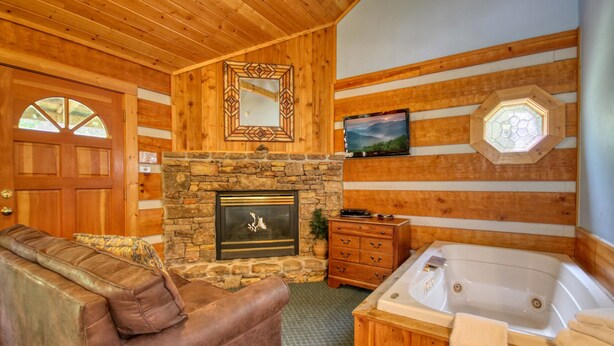 A wooden cabin interior with a stone fireplace, a wooden sofa, a wooden cabinet, and a large wooden-framed mirror. - Gatlinburg | Hot Tub | Pet Friendly | WiFi | Fireplace (GATLINBURG)