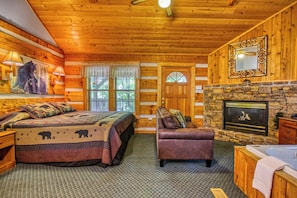 A log cabin bedroom with a bed, a sofa, a fireplace, and a stone wall.