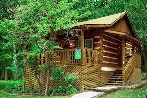 A wooden cabin with a porch, surrounded by trees.