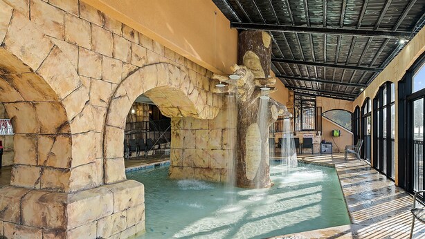 Un arco de piedra que da paso a una zona de piscina con una cascada.
