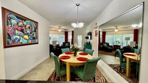 A dining area with a round table, green chairs, and a colorful abstract painting on the wall. - Updated Single Story Comal River Condo with Pool-Walk to Downtown NB (New Braunfels)