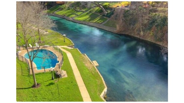 A river with a clear blue pool on the left, surrounded by a grassy area with a pathway. - Updated Single Story Comal River Condo with Pool-Walk to Downtown NB (New Braunfels)