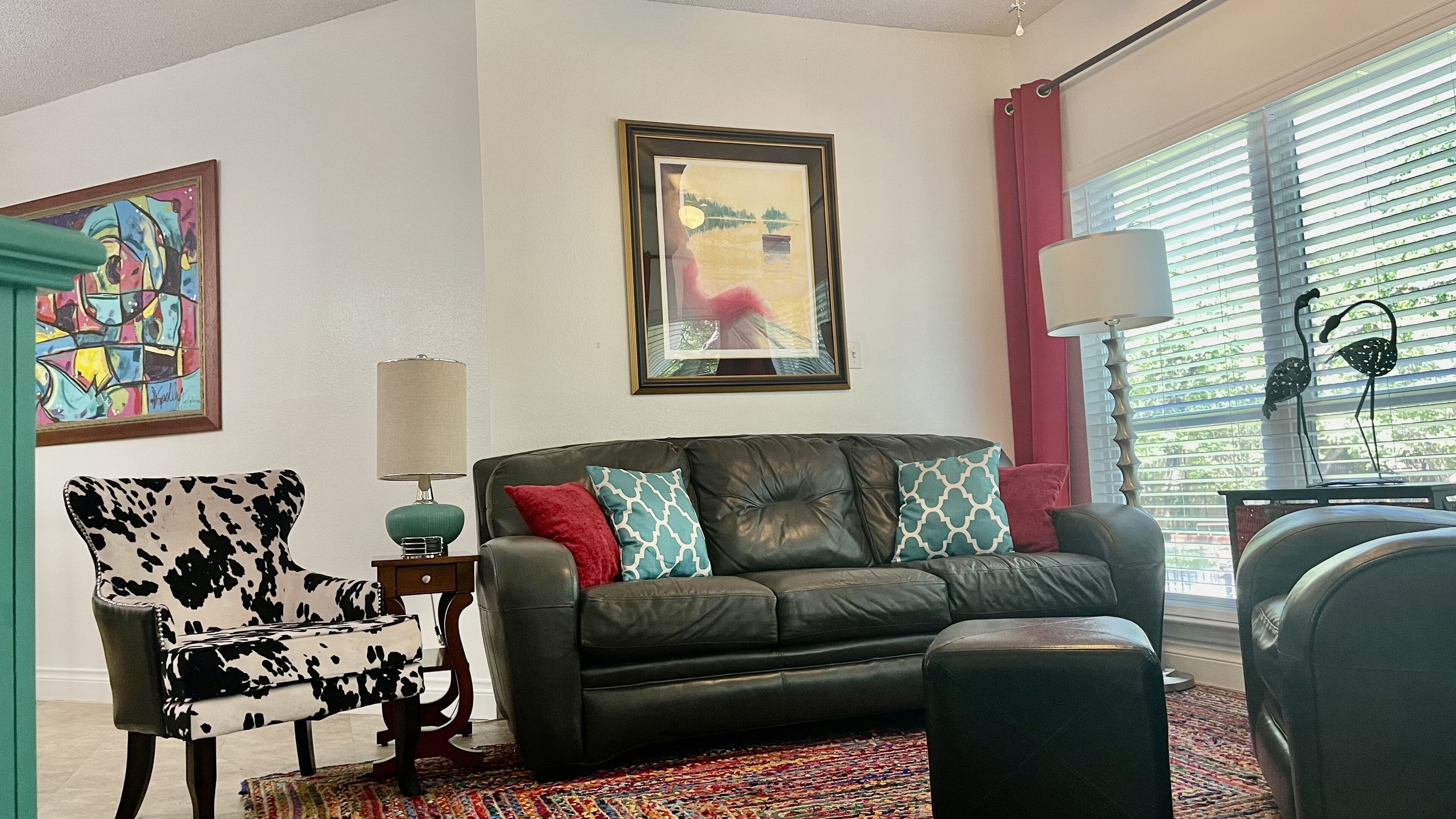 Un salon avec un canapé en cuir noir, un fauteuil à motifs, un tapis coloré, un tableau encadré et une lampe.