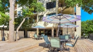An outdoor patio with wooden flooring, green metal chairs, and purple umbrellas. - Updated Single Story Comal River Condo with Pool-Walk to Downtown NB (New Braunfels)