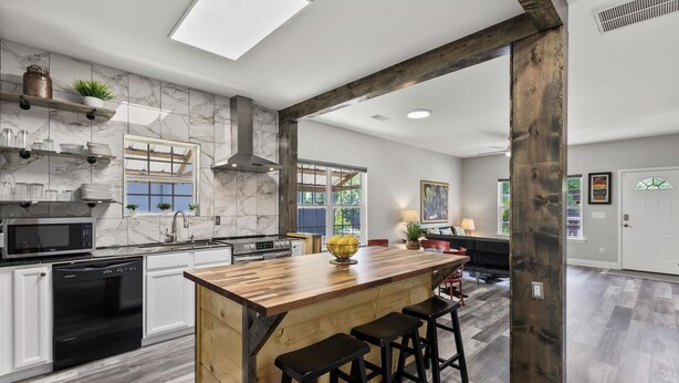 A modern kitchen with marble tiles, a wooden island with stools, and a large window.