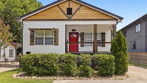 A single-story house with a red door, white siding, and a wooden front porch.