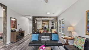 A modern living room with a black leather sofa, a wooden coffee table, and a dining area in the background.